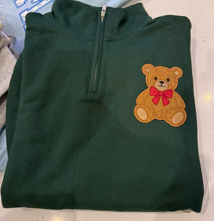 Folded forest green quarter zip sweatshirt showing the stand collar, front zipper and small teddy bear embroidery on the left chest.