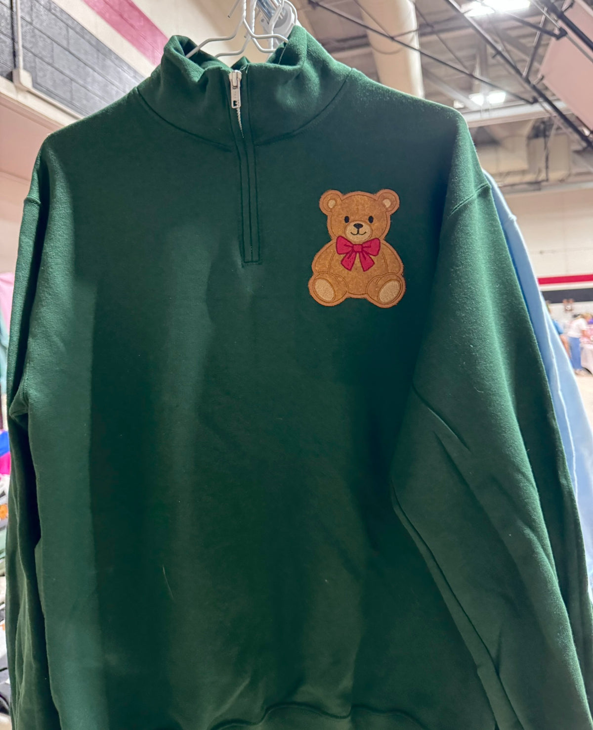 A forest green quarter zip sweatshirt with a brown teddy bear applique and red bow, highlighting the embroidered chest design.