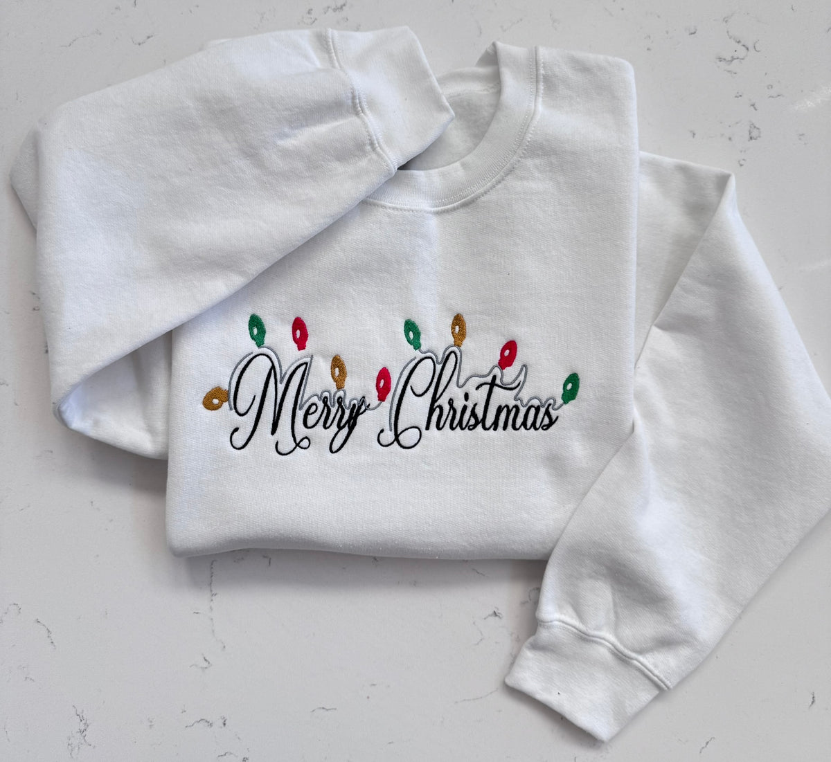 Close up of Christmas lights and Merry Christmas embroidery on white sweatshirt