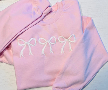 Pink sweatshirt with white coquette bow embroidery displayed flat