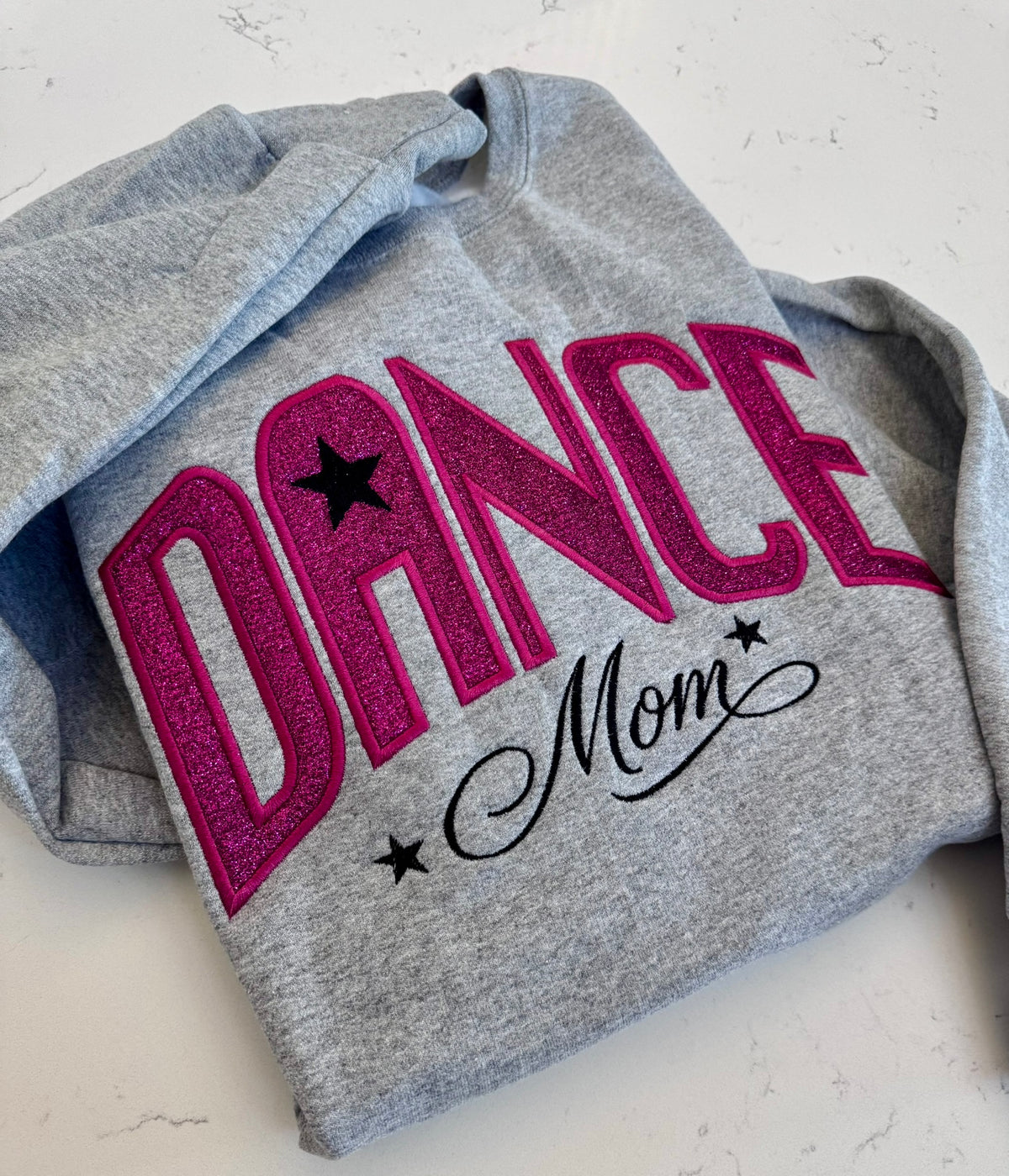 Close-up of hot pink sparkle DANCE appliqué on a gray embroidered sweatshirt