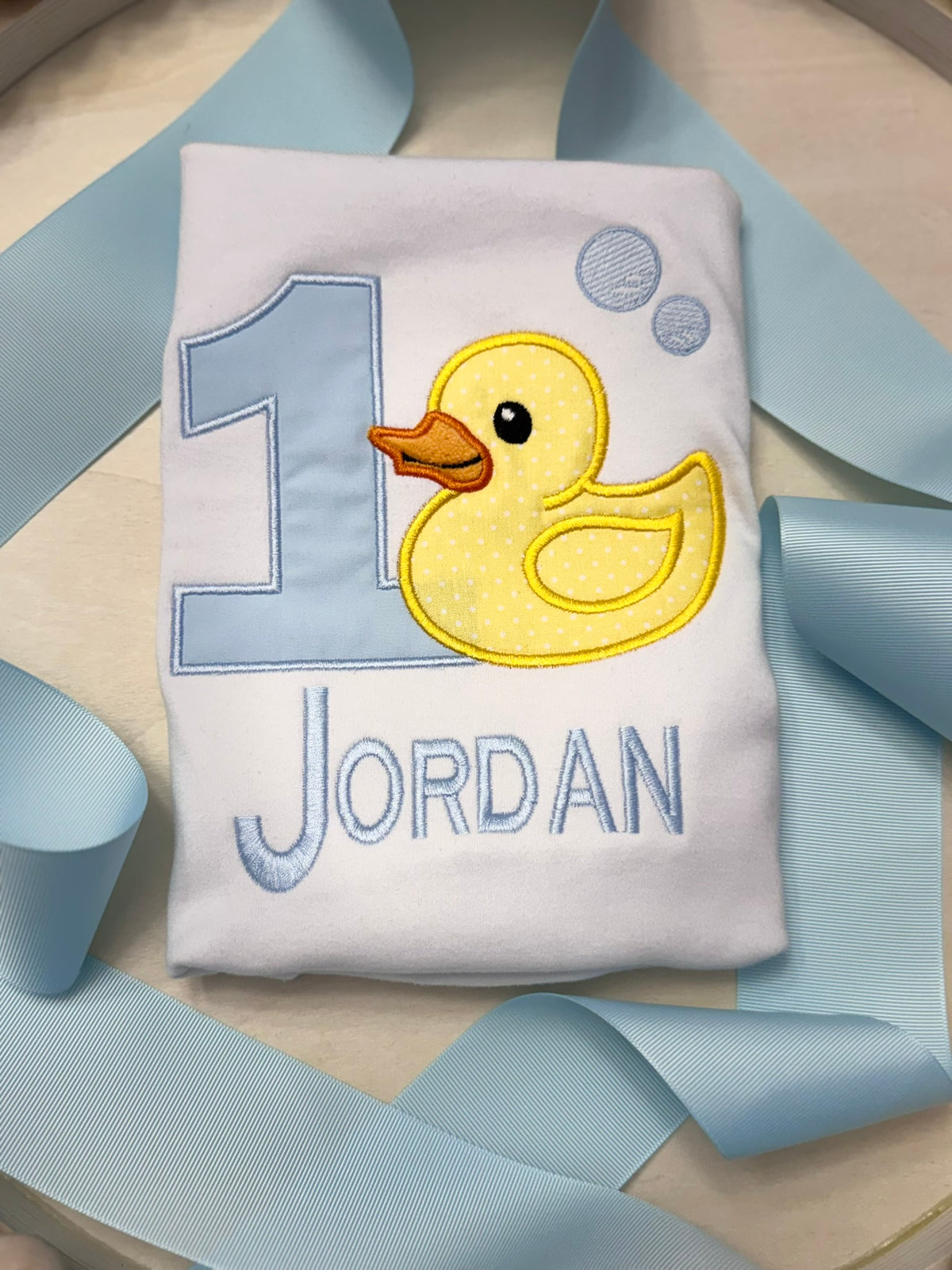 Close up of embroidered duck applique and blue birthday number on baby shirt