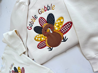 Detailed view of handmade Thanksgiving turkey fabric applique with burgundy gingham, mustard floral and black polka dot feathers.