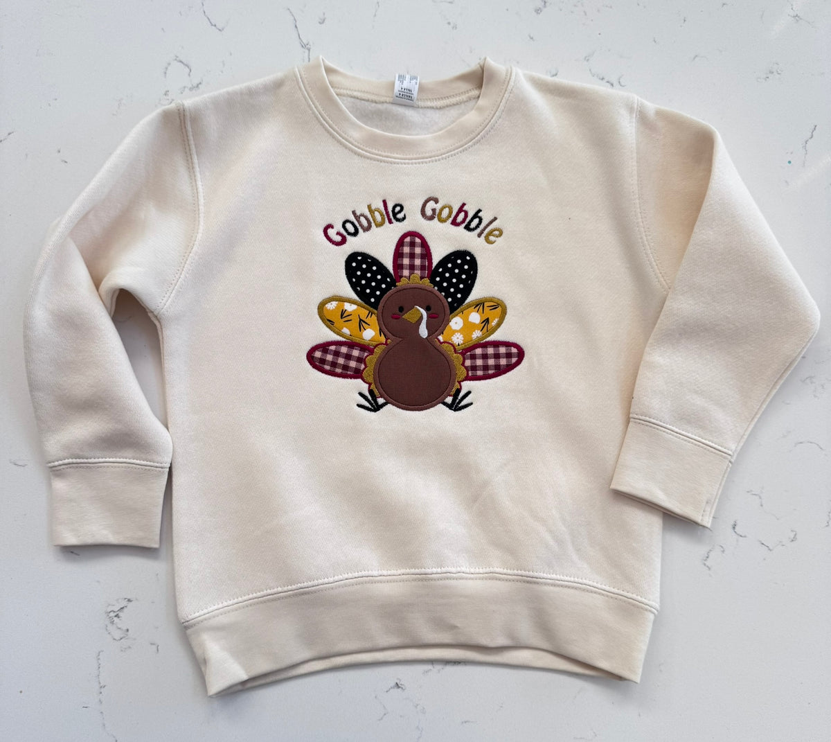 Cream toddler Thanksgiving crewneck sweatshirt with Gobble Gobble lettering and a colorful fabric applique turkey centered on the chest.