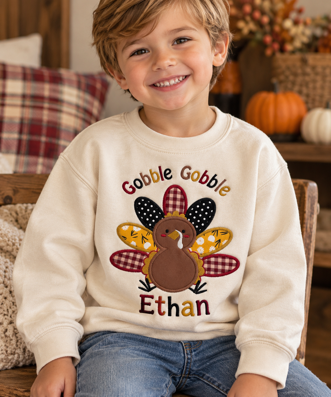 Smiling toddler boy wearing a cream Gobble Gobble Thanksgiving sweatshirt with colorful embroidered turkey applique and personalized name Ethan.