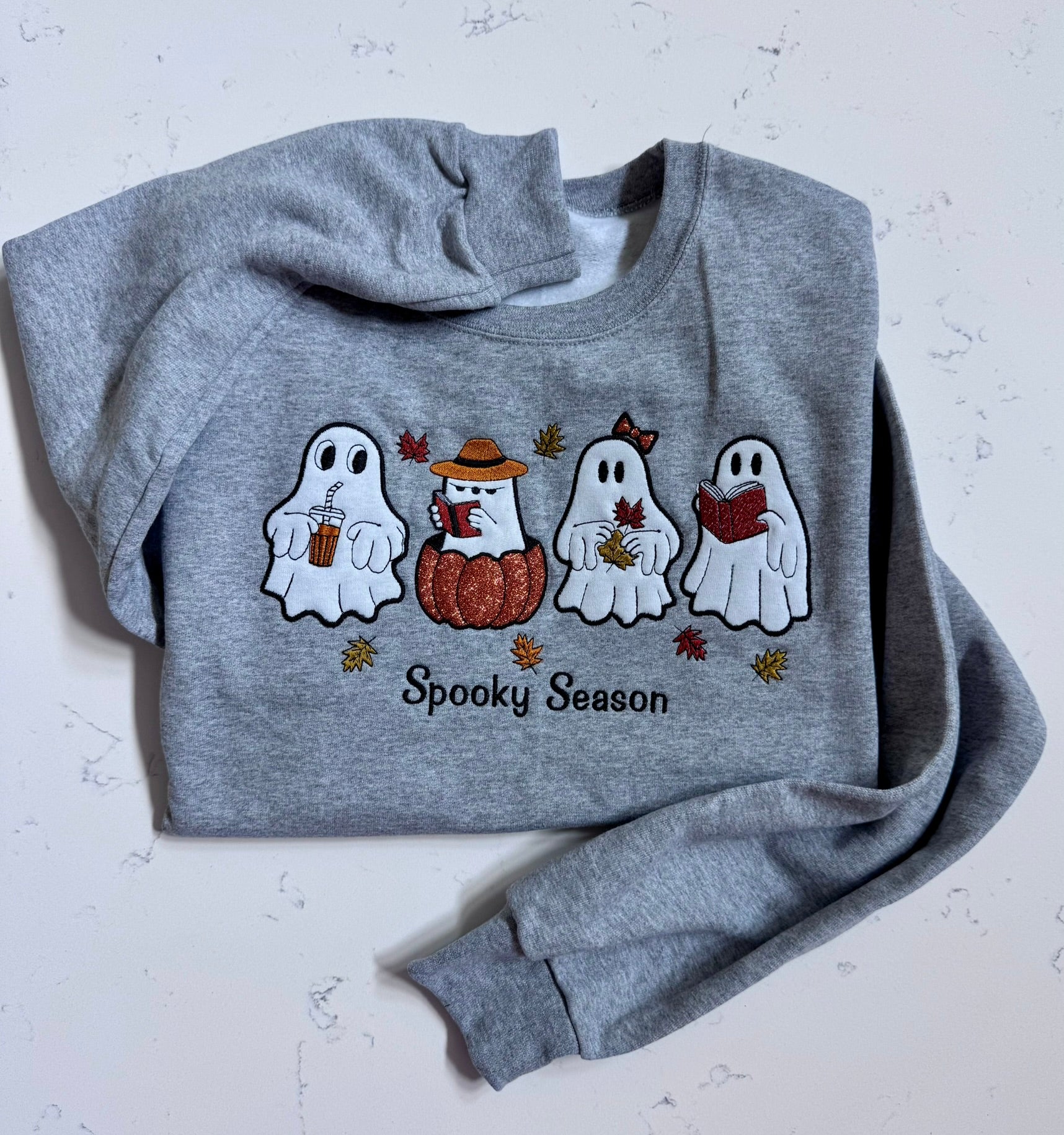 Spooky Season embroidered ghost sweatshirt in heather gray with four ghost characters holding coffee, reading books, and holding fall leaves