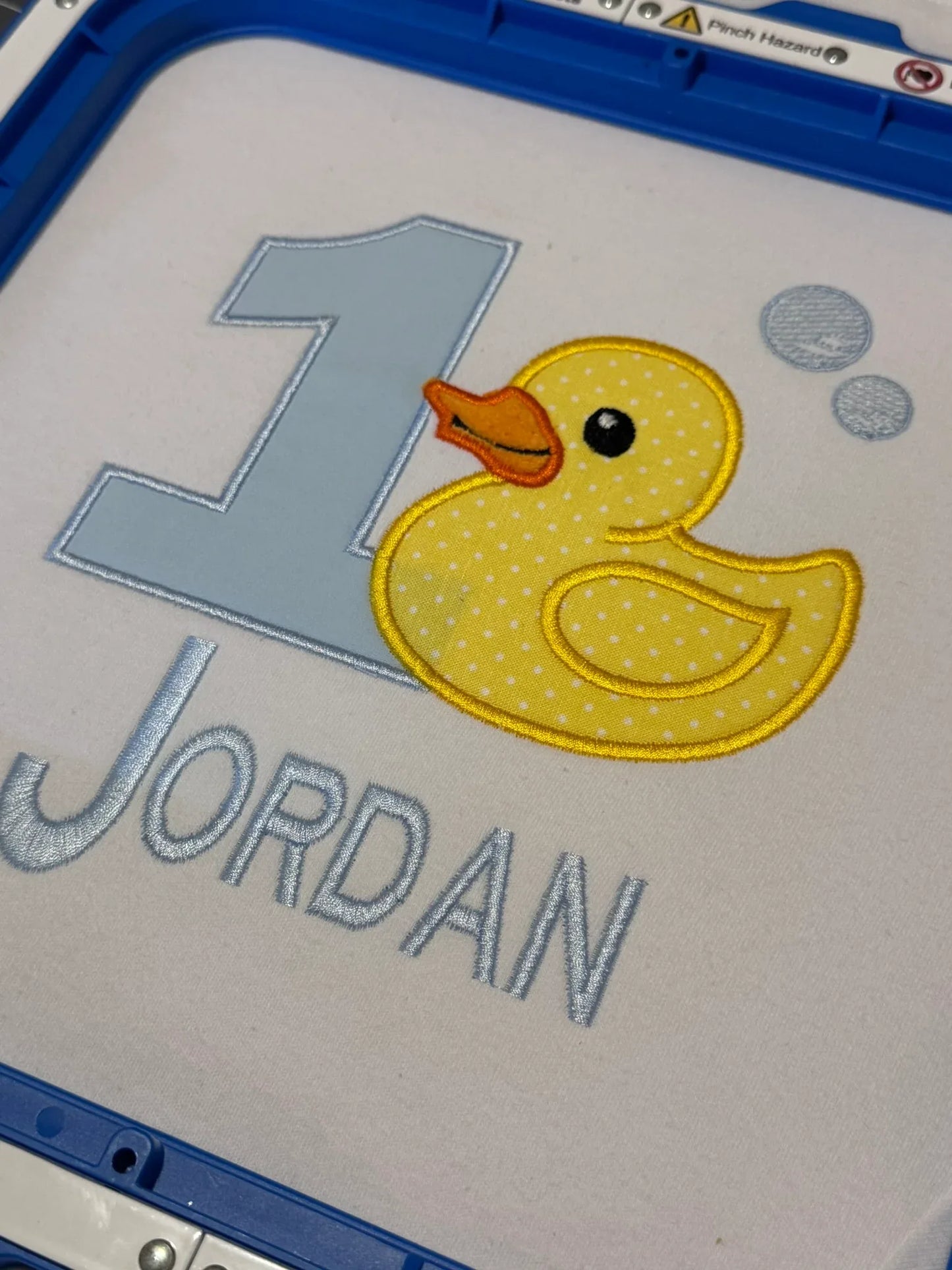 Detail of personalized duck embroidery on first birthday baby shirt