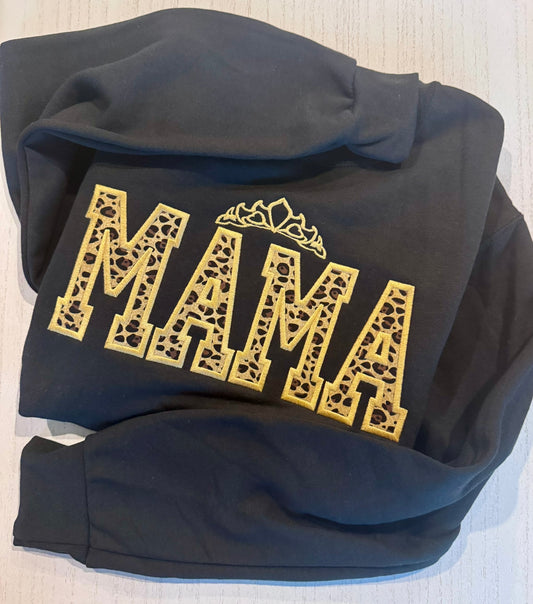 Black hoodie with 'MAMA' printed in leopard fabric and outline embroidered gold on a light background 