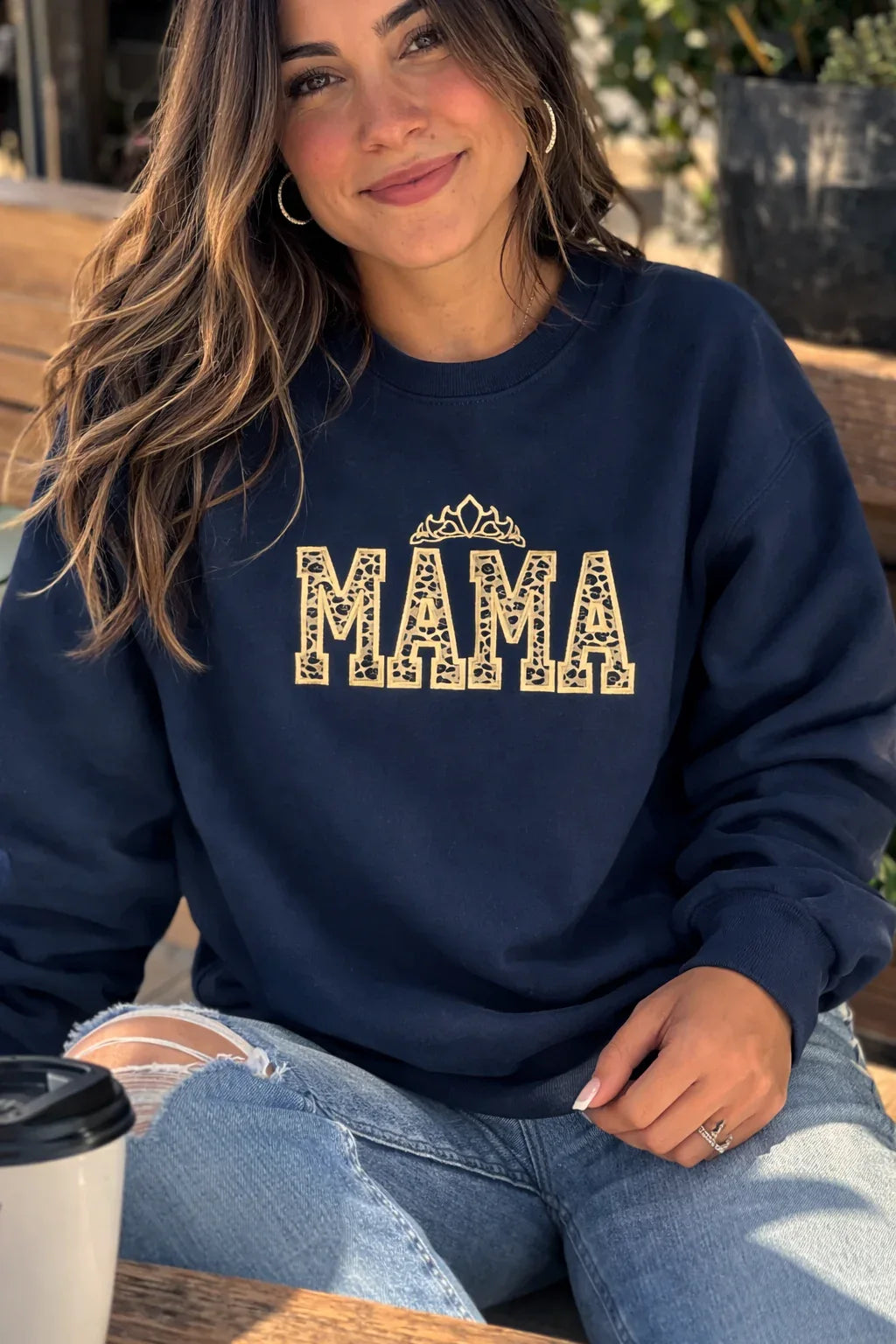 Woman wearing a black sweatshirt with 'MAMA' leopard embroidered applique with gold crown