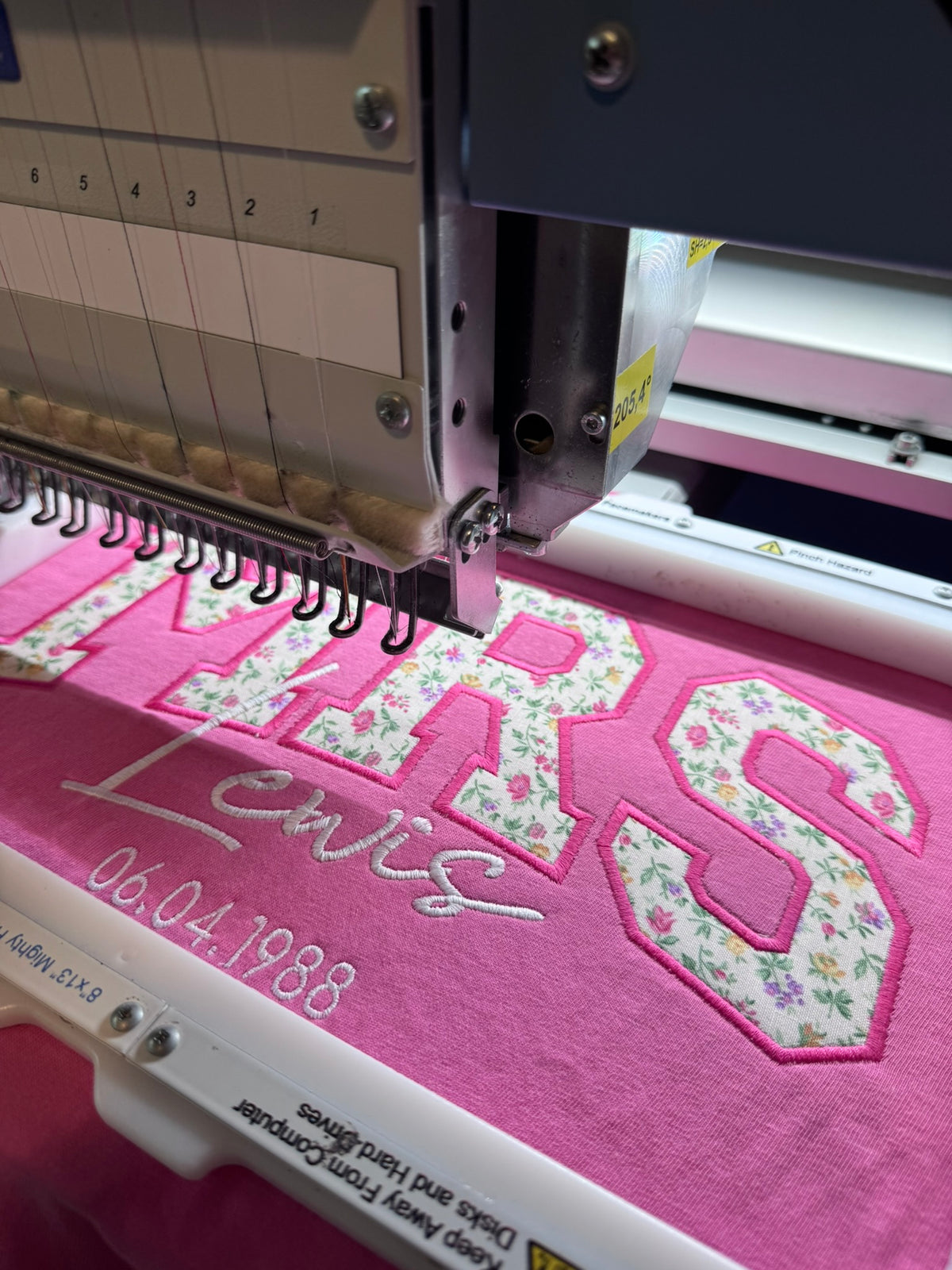 Personalized pink MRS appliqué shirt being professionally embroidered
