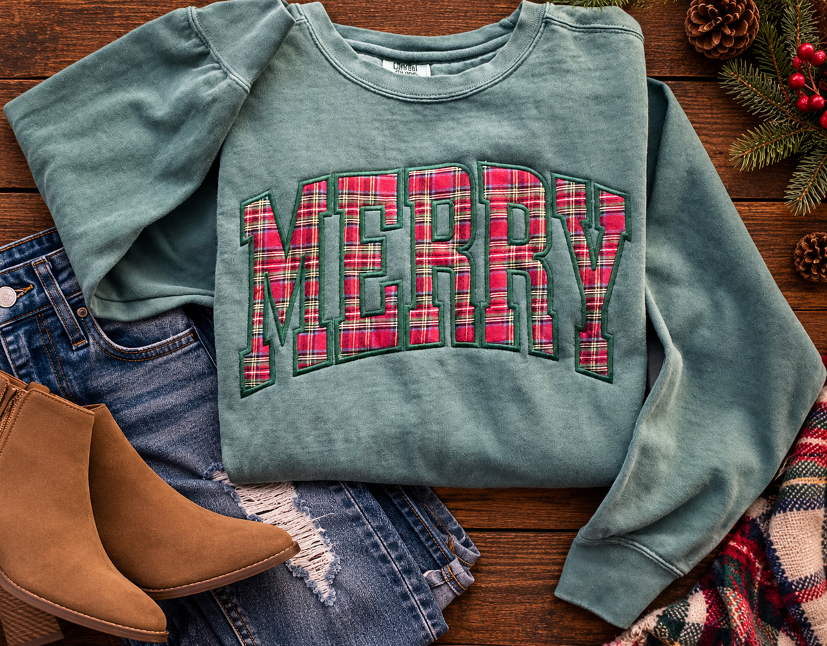 Flat lay of a light green MERRY plaid appliqué Christmas sweatshirt styled with jeans, booties and Christmas greenery.