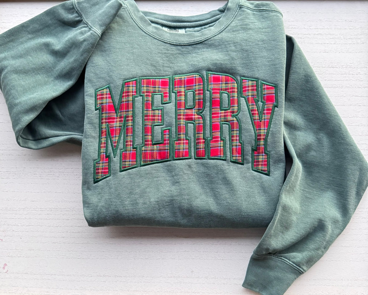 Folded light green Christmas sweatshirt with a red plaid MERRY appliqué and forest green embroidered outline.
