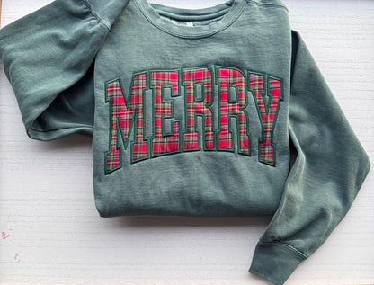 Light green Comfort Colors crewneck sweatshirt with a red plaid MERRY appliqué, folded on a white background.