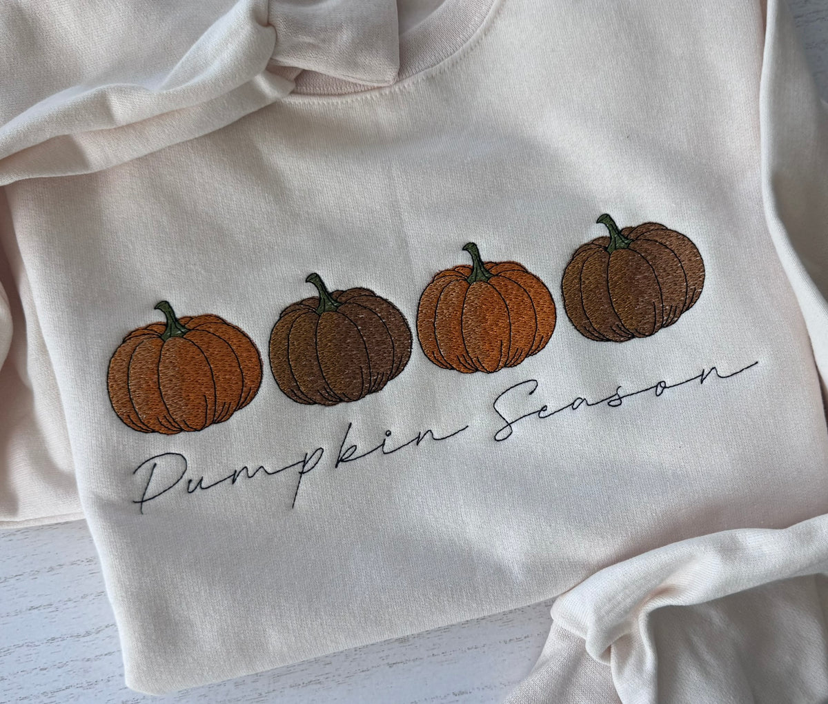 Close-up of three embroidered pumpkins on a cream fall sweatshirt