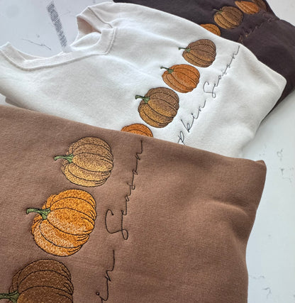 Cream and pecan Pumpkin Season sweatshirts with three embroidered fall pumpkins
