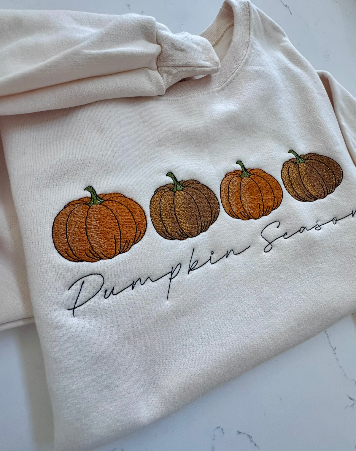 Cream sweatshirt featuring three embroidered pumpkins in autumn colors
