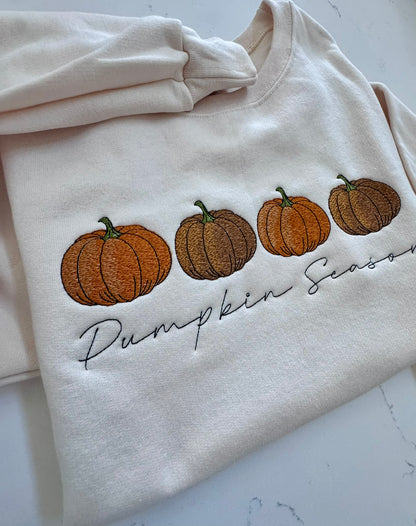 Cream sweatshirt featuring three embroidered pumpkins in autumn colors