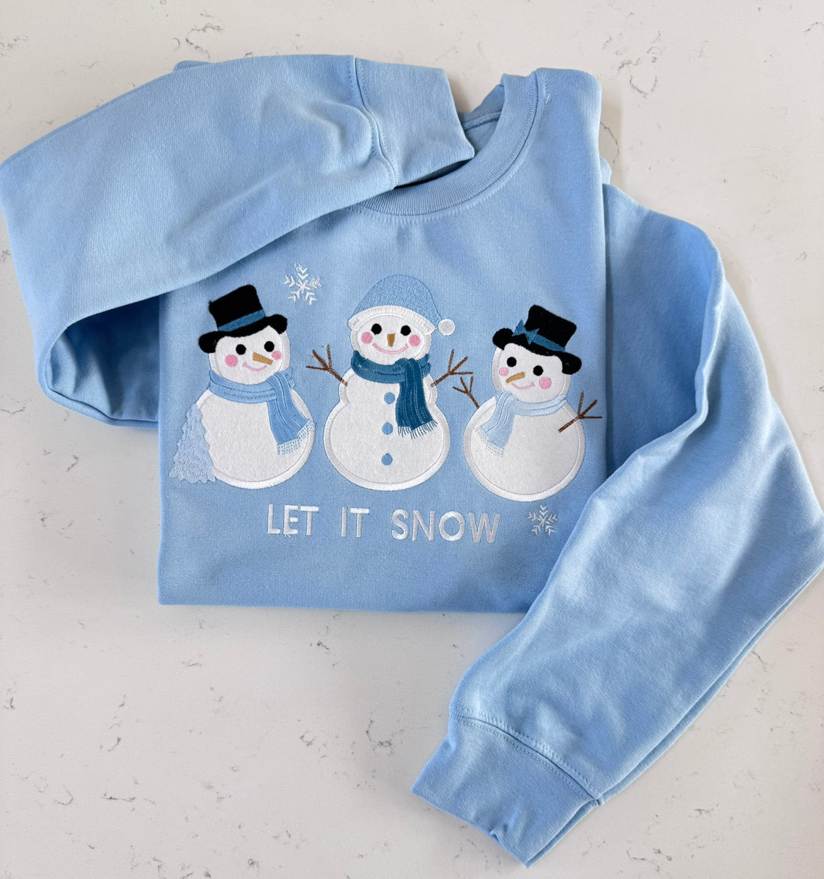 Light blue Let It Snow sweatshirt featuring three cute snowmen with detailed fabric appliqué and embroidery.