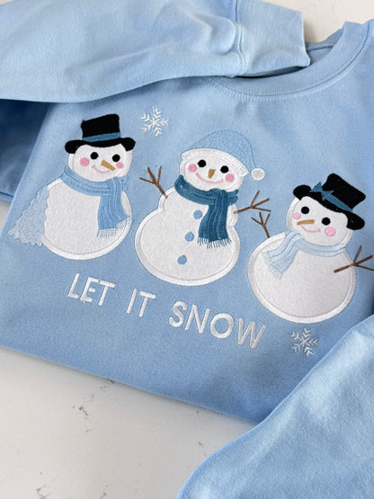Close-up of snowman appliqué embroidery featuring blue scarves, black hats, pink cheeks and snowflakes.