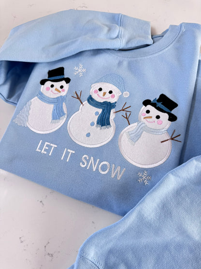 Detailed view of three snowmen with fabric appliqué, embroidered winter accessories and Let It Snow text.
