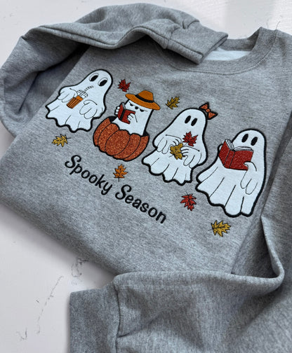 Close-up of colorful embroidered ghosts, pumpkin, coffee and books on gray sweatshirt