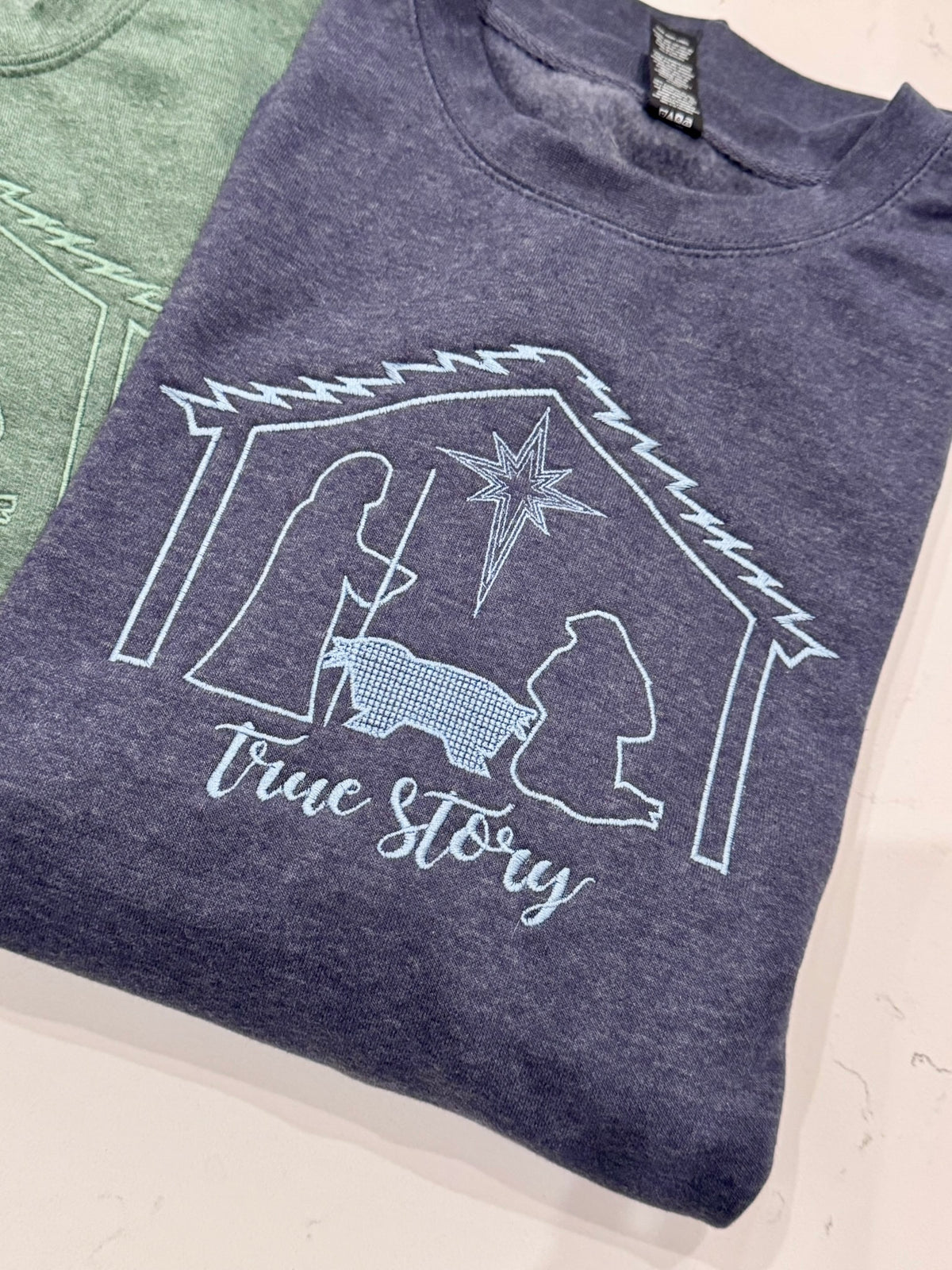 Close-up of embroidered manger scene and True Story lettering on a vintage heather navy sweatshirt.