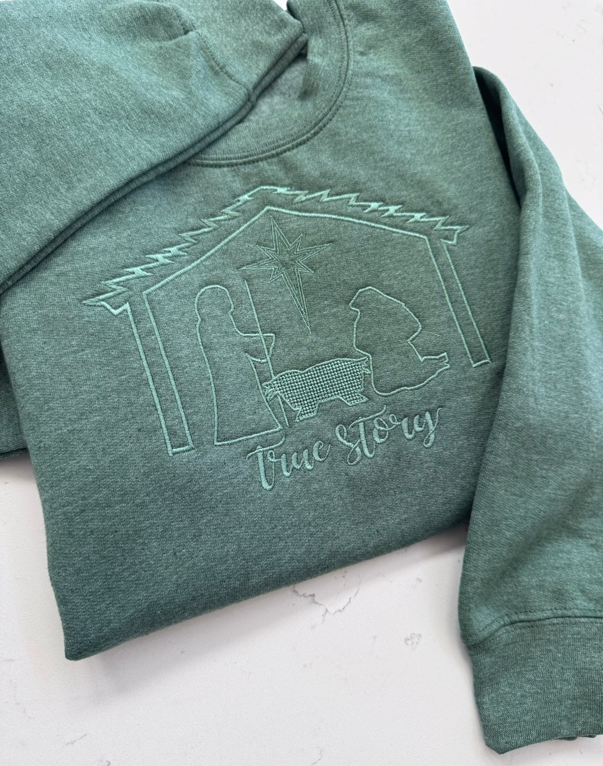 Heather dark green nativity sweatshirt with coordinating tonal embroidery of Mary, Joseph, baby Jesus and the Bethlehem star.