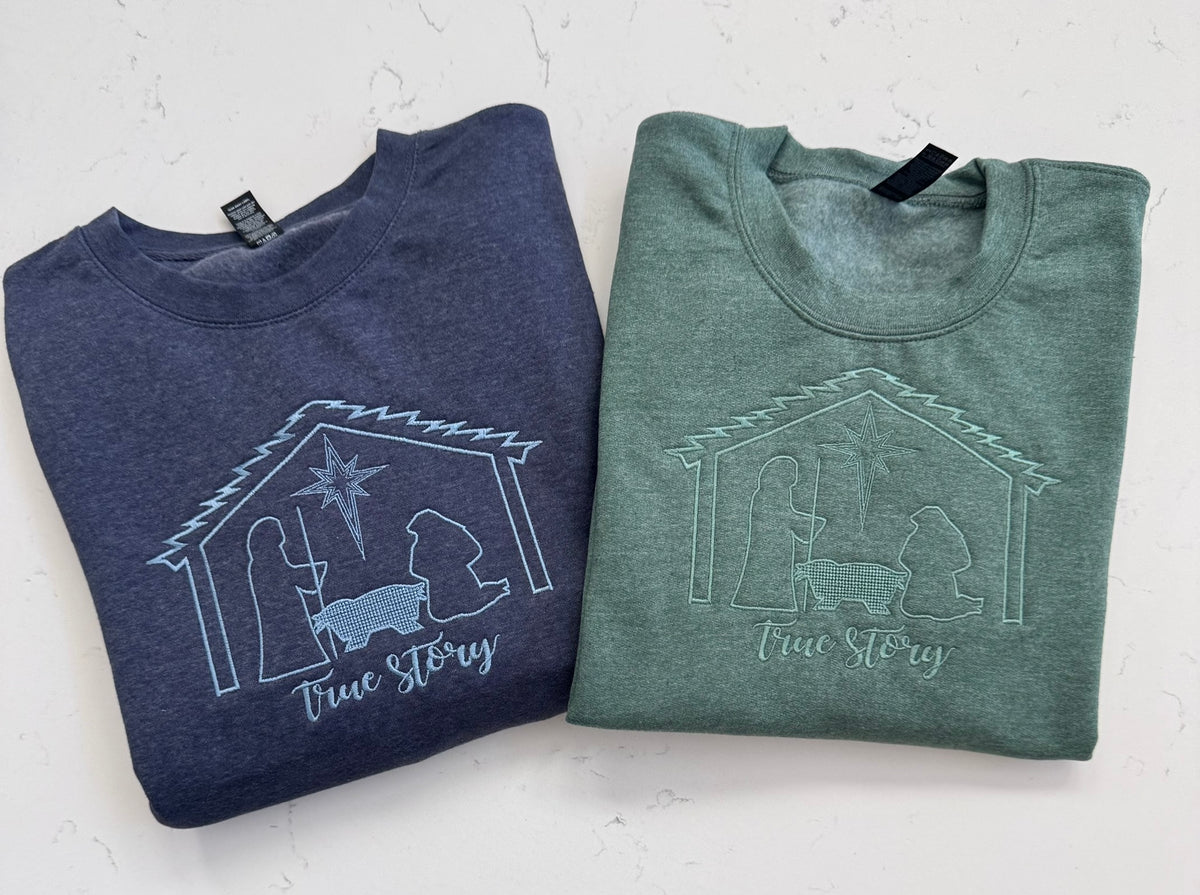 Heather dark green and vintage heather navy sweatshirts featuring the embroidered True Story nativity design.