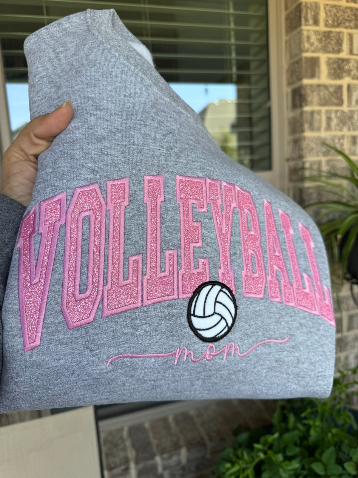 Close-up of pink sparkle VOLLEYBALL appliqué embroidered on a gray sweatshirt