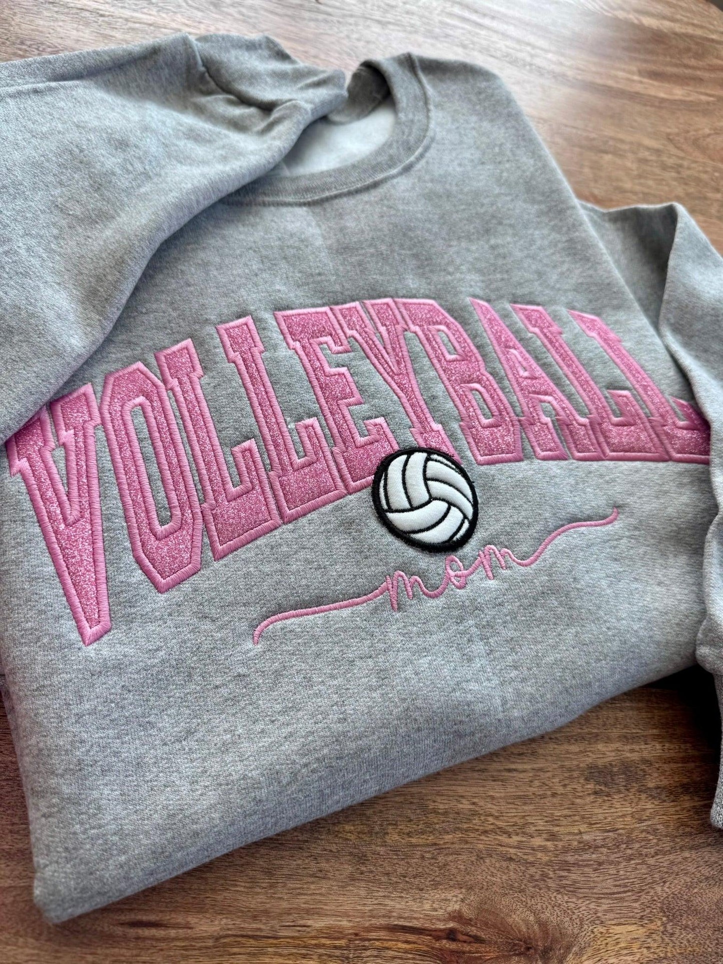 Gray sweatshirt with pink 'Volleyball' text and volleyball icon on a wooden surface