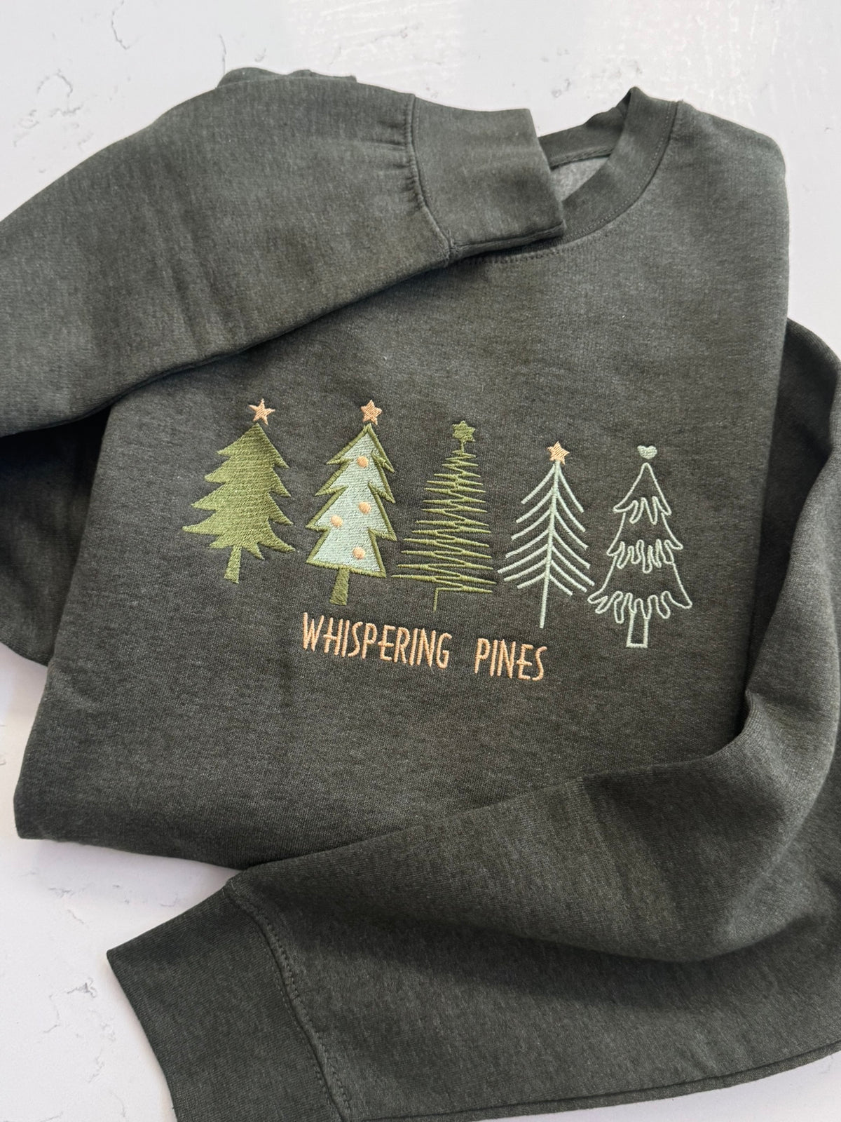 Close-up of Whispering Pines embroidered trees on a forest green heather sweatshirt