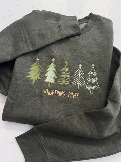 Close-up of Whispering Pines embroidered trees on a forest green heather sweatshirt