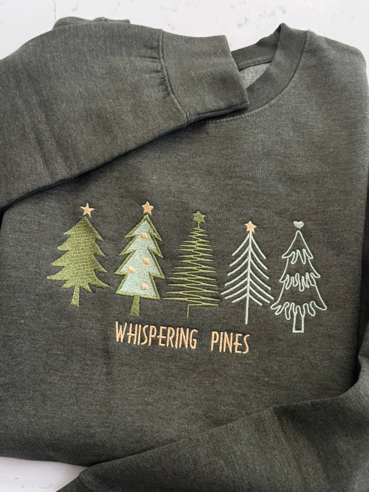 Folded forest green heather sweatshirt with embroidered pine trees and Whispering Pines wording