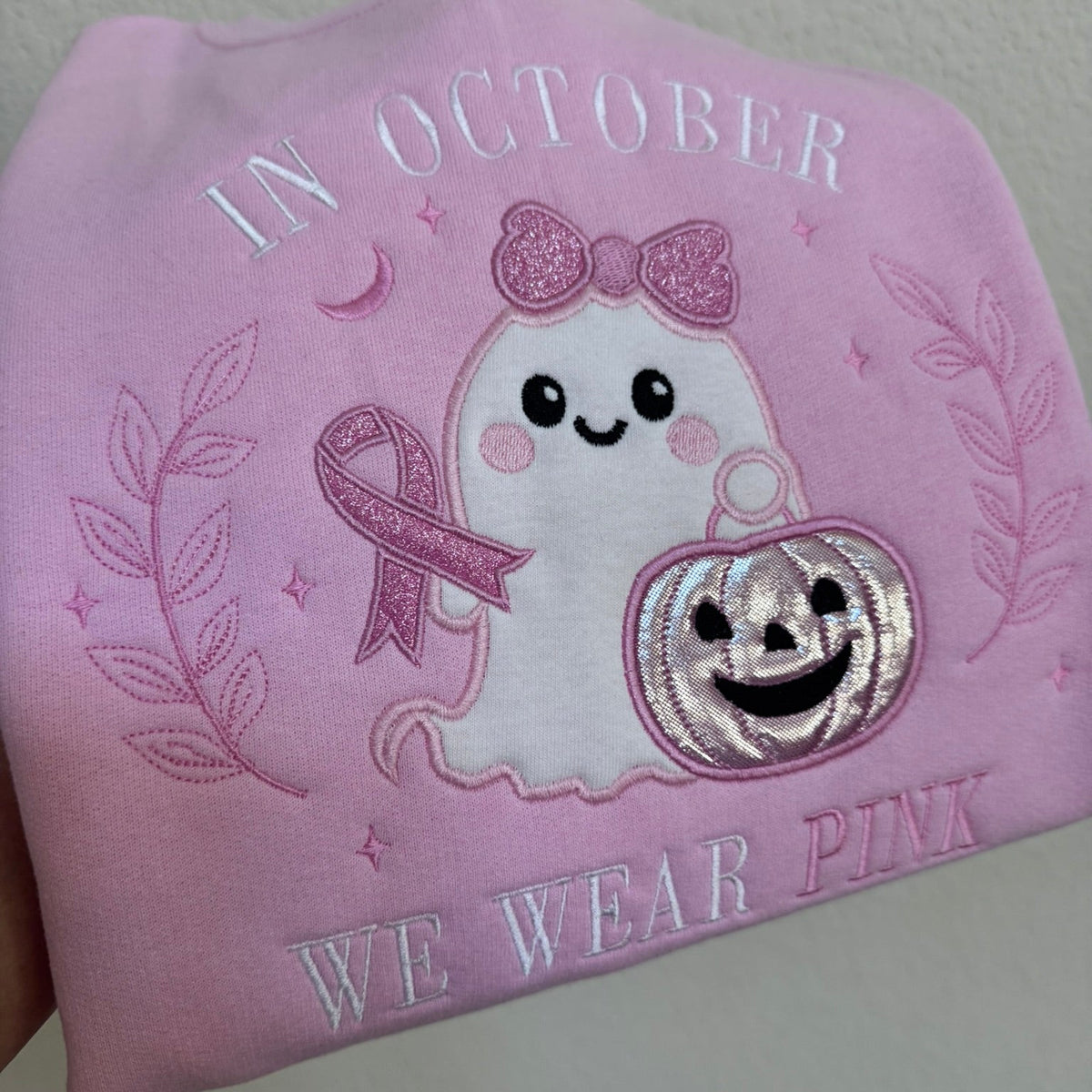Close-up of embroidered ghost, pink ribbon and pumpkin appliqué on pink sweatshirt
