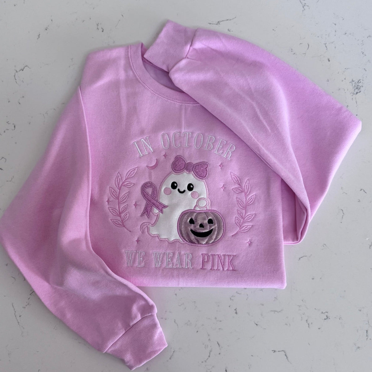 Folded pink sweatshirt featuring the In October We Wear Pink ghost design