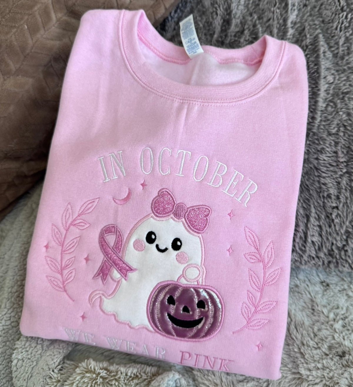 Pink sweatshirt displaying the embroidered breast cancer awareness ghost design